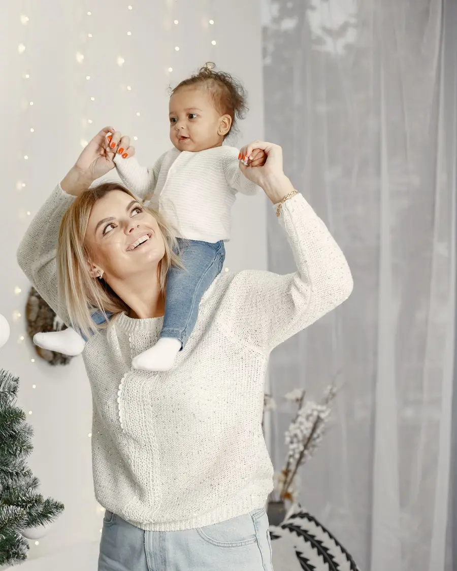 Mutter hebt ihr Kind vor dem Weihnachtsbaum in die Luft