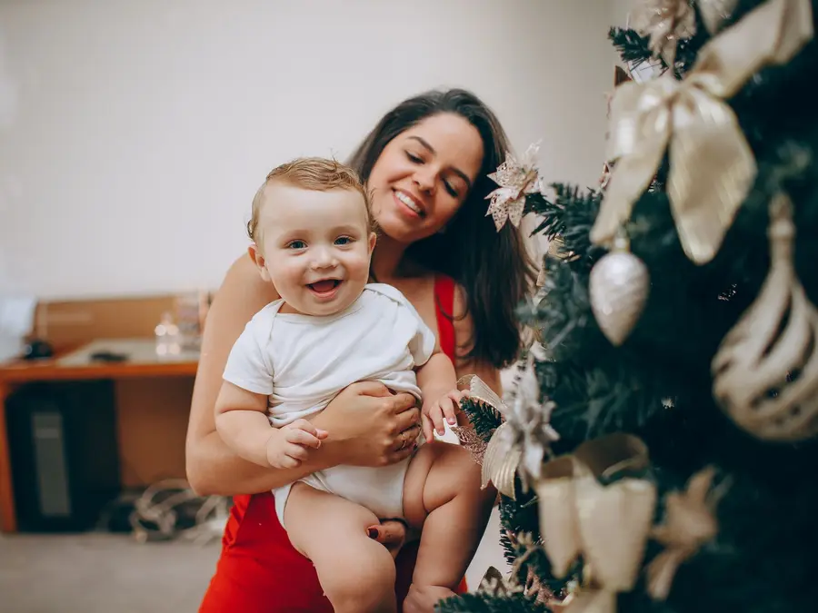 Mutter mit Baby neben dem geschmückten Weihnachtsbaum